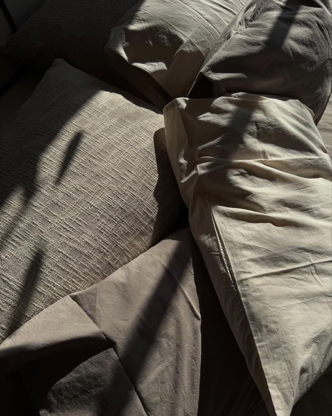 Neutral TAMEKO linen bedding and pillows in natural sunlight, textured and inviting bedroom scene.