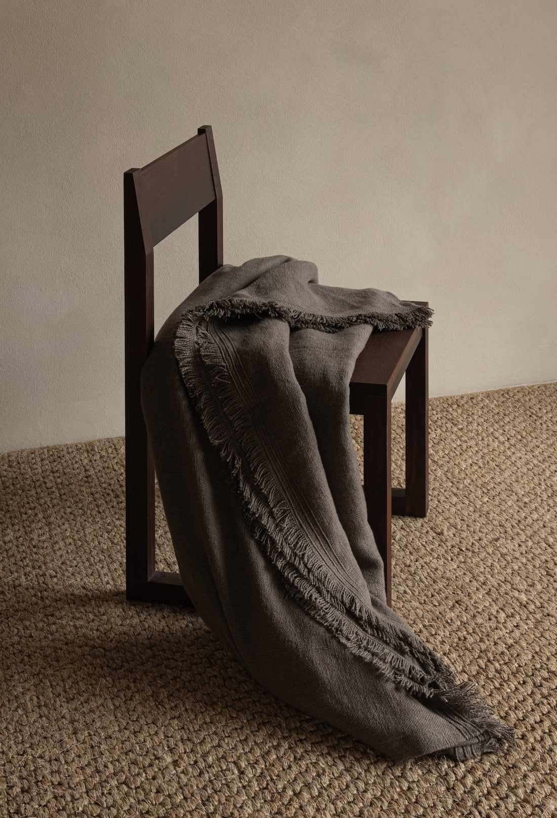 Dark woven throw blanket with fringed edges draped over a wooden chair on a textured rug, TAMEKO home decor