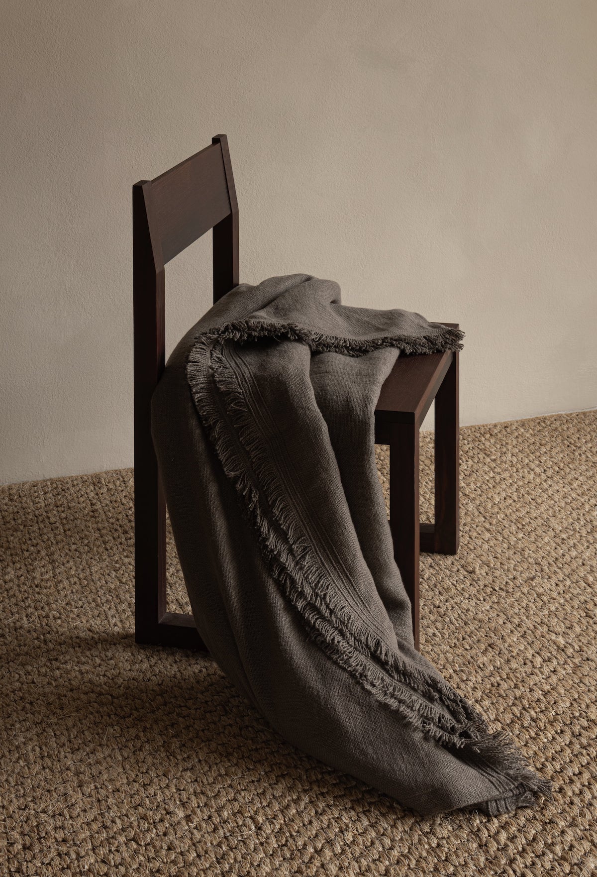 Dark woven throw blanket with fringed edges draped over a wooden chair on a textured rug, TAMEKO home decor