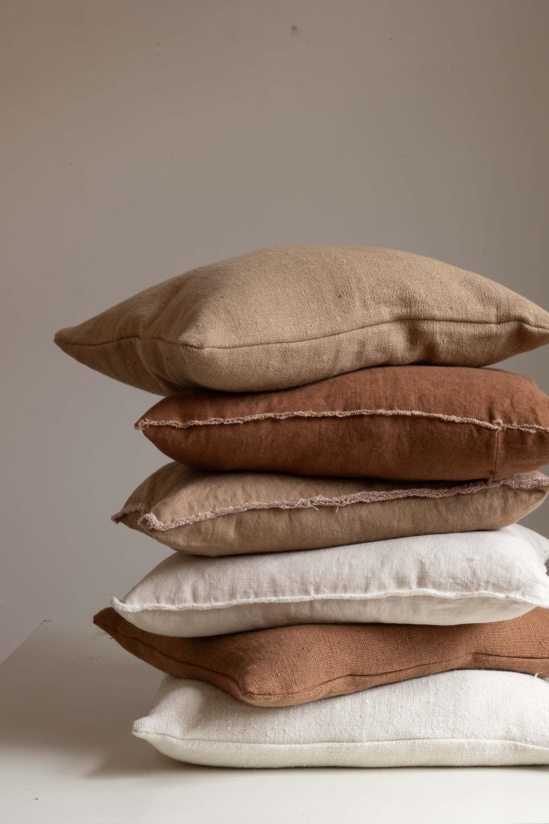 Stack of neutral-toned linen and cotton TAMEKO cushions on a white surface