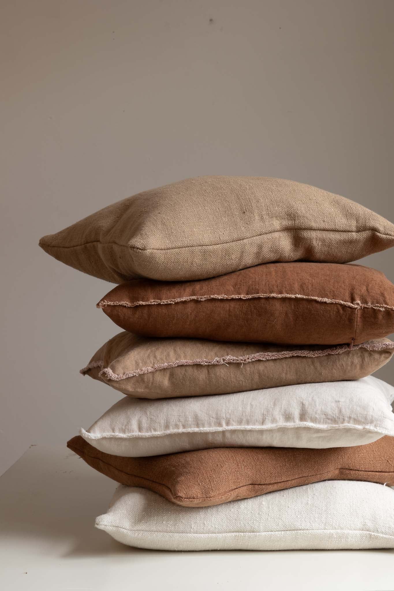 Stack of neutral-toned linen and cotton TAMEKO cushions on a white surface