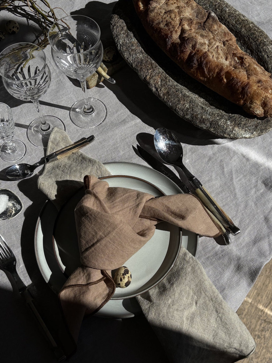 Elegant table setting with linen tablecloth, crystal glasses, artisanal bread, and natural napkins