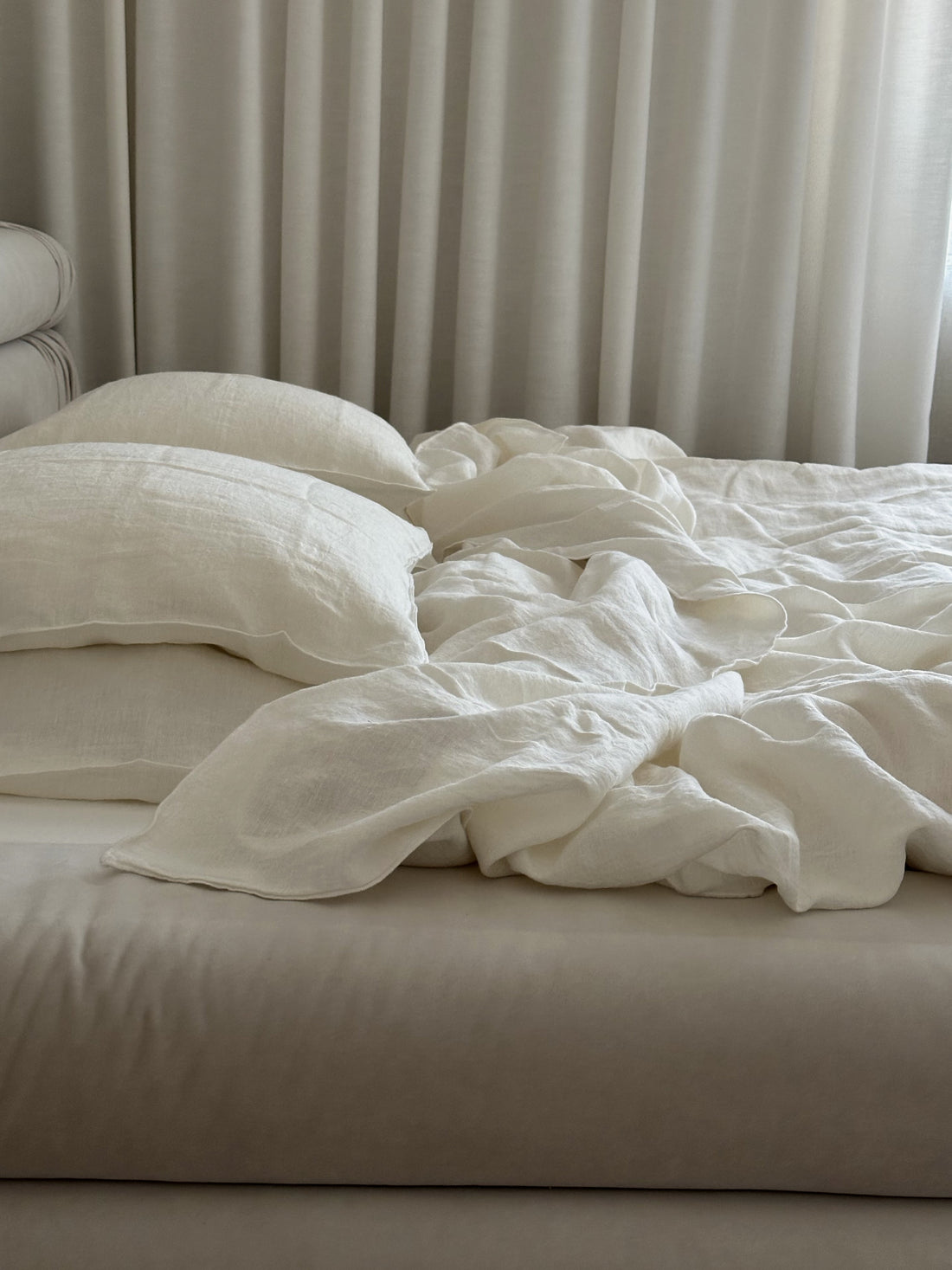 Soft natural linen bed sheets and pillows on an unmade bed, neutral modern bedroom.