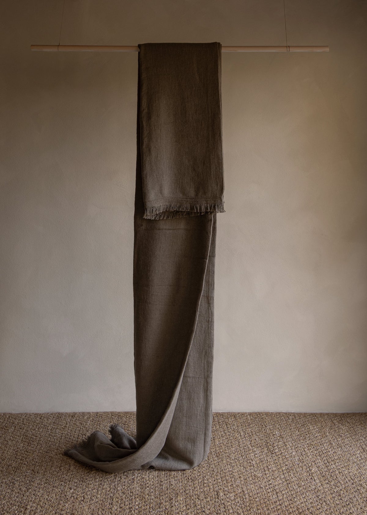 Neutral-tone linen bed throw with fringed edge hanging indoors on wooden rod, TAMEKO home textile