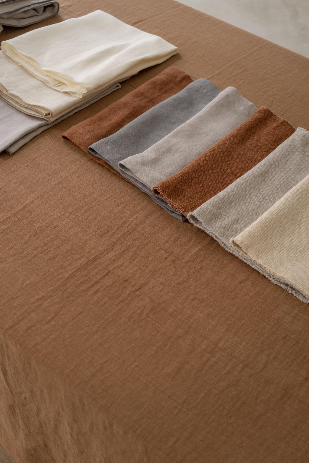 Neutral earth-toned TAMEKO linen fabric swatches neatly folded on a brown tablecloth.