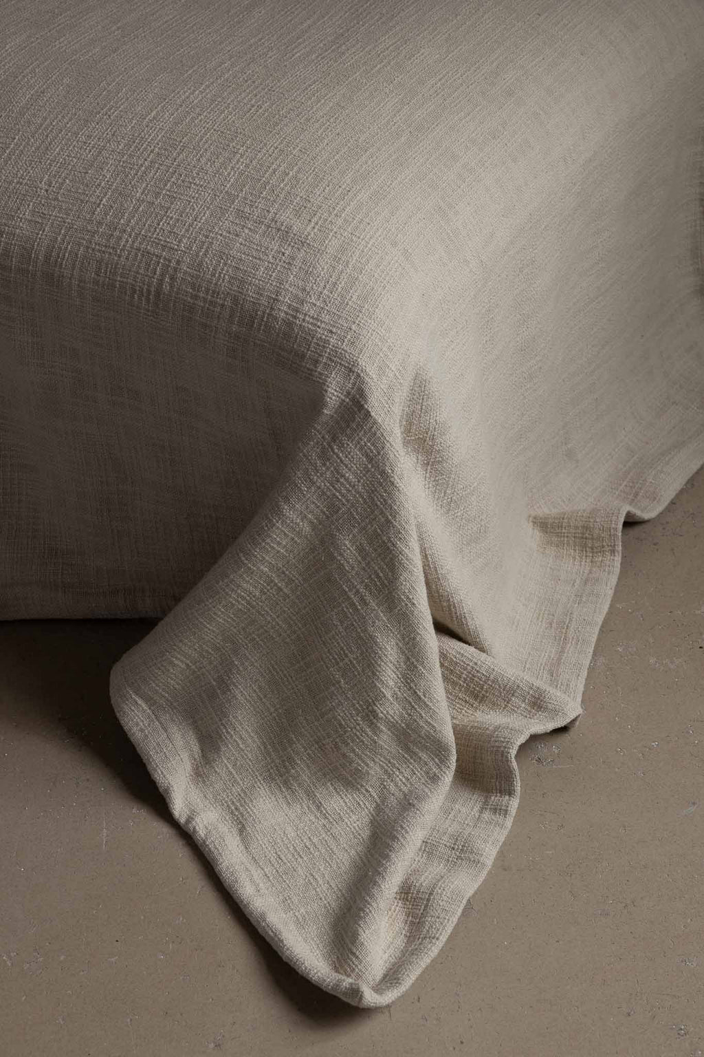 Textured natural linen fabric draped over a bed corner on neutral flooring, TAMEKO home decor