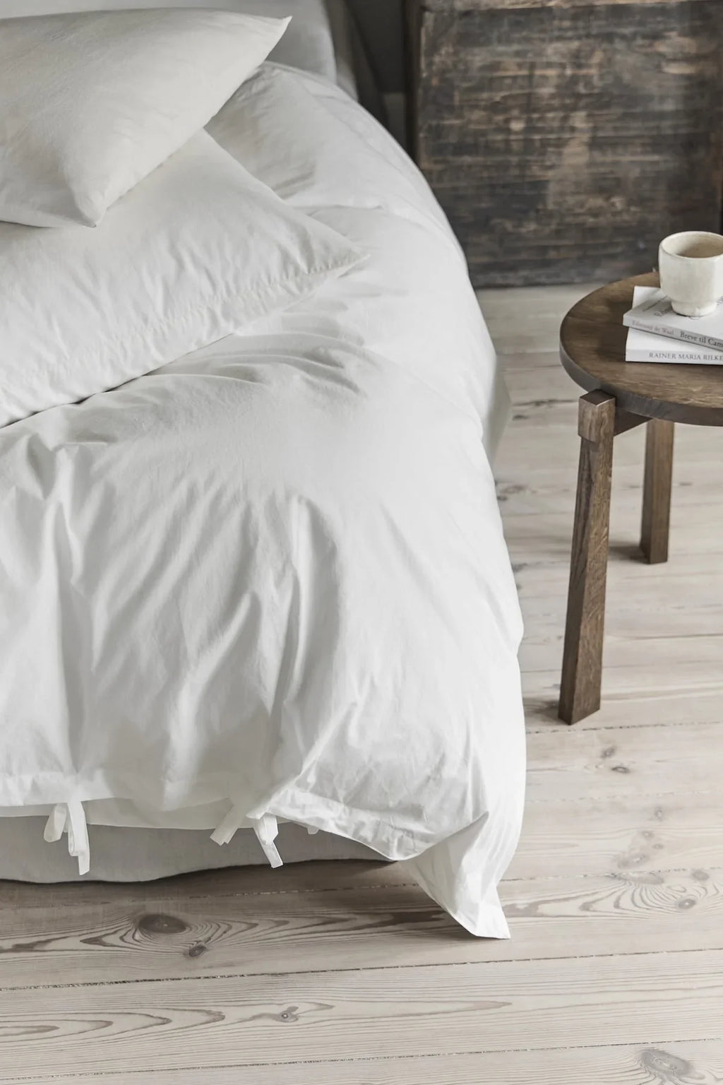 TAMEKO white bedding set on bed with pillows, wooden nightstand, cup, and books