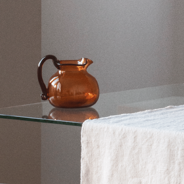 Brown glass pitcher on a clear table with beige linen tablecloth, TAMEKO home decor